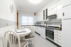 a white kitchen with a table and chairs at Encantador piso con parking by CABANA Rentals in Vigo +14 photos