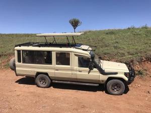 a white jeep with a surfboard on top of it at silver travel sand safari in Ngambo