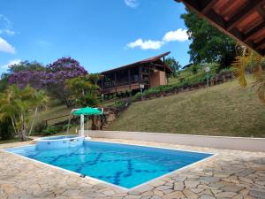 a pool with an umbrella and a house in the background at Pousada Colar de Ouro in Cunha