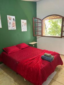 a bedroom with a bed with a red comforter and a window at Pousada Flor da Mata in Nova Lima