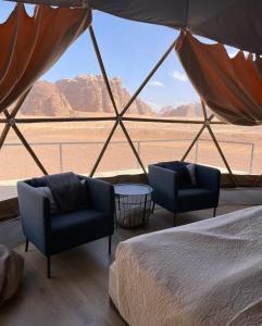 una camera con due sedie e un letto e vista su un deserto di RUM CAMILLA lUXURY CAMP a Wadi Rum