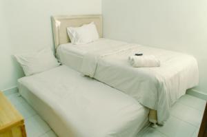 two beds with white sheets and a towel at Comfort Studio Apartment Aeropolis Residence By Travelio in Tangerang