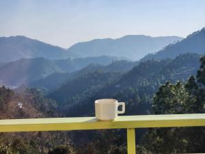 a cup of coffee sitting on a railing overlooking a mountain valley at Mountain Golden Ray in Mukteswar
