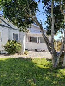 a white house with a tree in the yard at 5 Bedroom House A with 13 Beds including 6 Double Beds, 2 Single Beds, and 5 Sofa Beds in Auckland