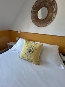 a white bed with a yellow pillow and a mirror at Hôtel Restaurant La Voile Bleue in Erdeven