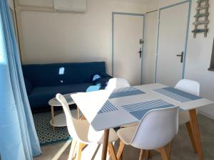 a dining room table with white chairs and a blue couch at Joli Duplex résidence Atlantis accès direct plage in Le Barcarès