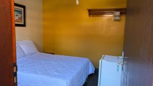 a small bedroom with a bed and a refrigerator at Suites Casa Amarela in Cabo Frio