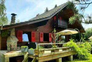 a house with red shuttered windows and a deck at Confortable chalet au calme à l'étang du stock in Langatte