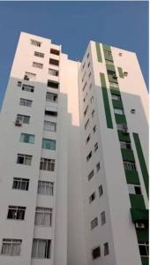 a tall white building with green windows on it at Apto 2 quartos em frente à praça nova do Imbui Excelente localização in Salvador