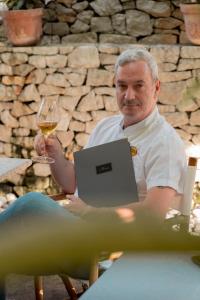 a man sitting in a chair with a glass of wine and a laptop at Locanda Gaudemus Boutique Hotel in Sistiana