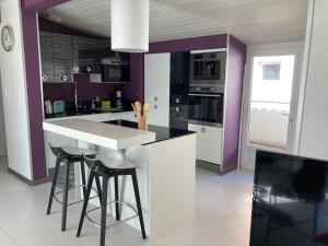 eine Küche mit weißen und violetten Wänden und Hockern in der Unterkunft Pitchounette villa Canaulaise 3ch 8p in Lacanau