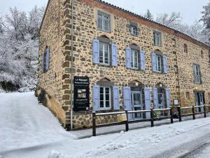 a brick building in the snow next to a street at Le Matagot Auberge-Restaurant in Mazeyrat-Aurouze