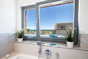 La salle de bains est pourvue d'une baignoire et de 2 fenêtres ornées de plantes. dans l'établissement Ostsee - Appartement Nr 80 "MeerSinn" im Strand Resort, à Heiligenhafen