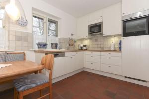 a kitchen with white cabinets and a wooden table at Hüs an den Salzwiesen in Borgsum