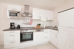 a white kitchen with white cabinets and appliances at D4 Bungalow - Haus Dünenpark Königsberger Allee 12 - FERIENDOMIZIL HOLLICH in Grömitz
