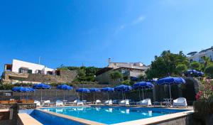 a swimming pool with blue umbrellas and chairs and tables at Hotel Punta Imperatore in Ischia