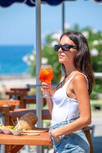 Eine Frau mit Sonnenbrille hält ein Getränk an einem Tisch. in der Unterkunft Hotel Punta Imperatore in Forio d'Ischia