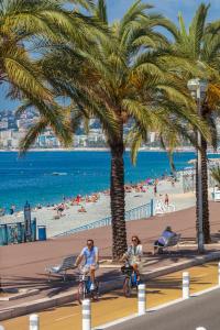 two people riding bikes on the beach under a palm tree at Le Campus Appartement in Nice