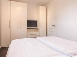 a white bedroom with a bed and a tv at Ferienwohnung Julian in Hörnum