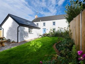 a white building with a black roof and a yard at Dyffryn Cottage in Cardigan
