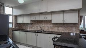 a kitchen with white cabinets and a black counter top at Peacehaven Beachfront Apartment - Scottburgh KZN in Scottburgh