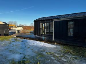 a black house with snow on the ground at Willa Rauha 1A, minikoti katetulla terassilla, ei saunaa in Lumijoki