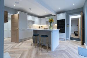 una cucina con armadi bianchi e un'isola con sgabelli di Lace Maker's Cottage a Keyworth