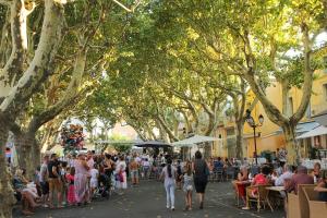 a crowd of people walking down a street with trees at Maison village in Sérignan