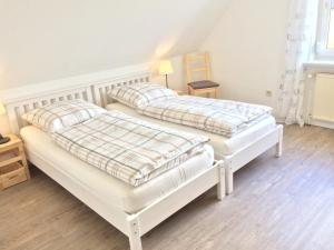 two white beds in a room with wooden floors at FeWo "Ahrens' Hüs" in Elsdorf-Westermühlen
