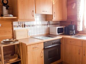 a kitchen with wooden cabinets and a stove and microwave at Ferienhaus Nr 15, Typ A, Feriendorf Jägerpark, Bayerischer Wald in Prackenbach