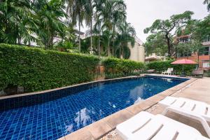a swimming pool with white lounge chairs next to a hedge at Jinta Andaman in Kata Beach