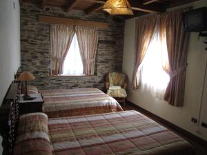 a bedroom with a bed and a chair and two windows at A Lareira in Chan de Vilar