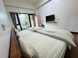 two beds in a bedroom with a tv on the wall at 明月大船的家民宿 in Chiayi City