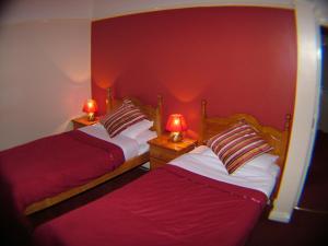 two beds in a room with red walls and two lamps at Gateway Lodge in Speke