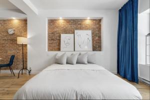 une chambre avec un lit blanc et un mur de briques dans l'établissement Initial / Suite trésor / Centre-Ville de Québec, à Québec