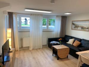 a living room with a black couch and two windows at Haus Ostwind - Wohnung 3 in Dahme