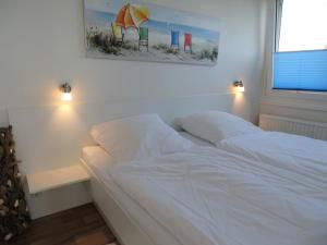 a white bed in a bedroom with a picture on the wall at Haus Wildfang FeWo 2 in Dahme +11 photos