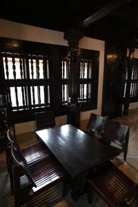 einen Holztisch und Stühle in einem Zimmer mit Fenstern in der Unterkunft Heritage Villa in Mangaluru + 16 Fotos