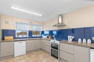 a large kitchen with white cabinets and blue walls at Fairways View at Haverfordwest Golf Club in Haverfordwest