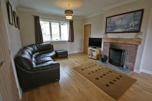een woonkamer met een leren bank en een open haard bij Heatherlea Holiday Cottage in Otterburn