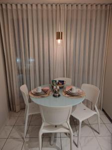 a table with white chairs and a table with plates and cups at Flat charmoso vista mar in Recife