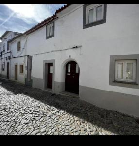 a white building with two doors on a cobblestone street at Casinha do Pão Bolorento in Évora