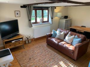a living room with a leather couch and a flat screen tv at The Quintessential Dorset Cottage in Lytchett Matravers