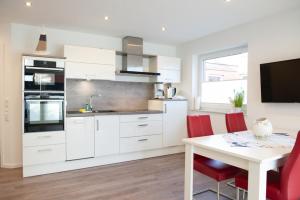 a kitchen with white cabinets and a table with red chairs at Deichnähe - G in Norddeich