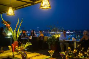um grupo de pessoas sentadas em mesas em um restaurante à noite em The Frangipani Royal Palace Hotel em Phnom Penh