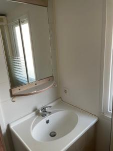 ein Badezimmer mit einem weißen Waschbecken und einem Spiegel in der Unterkunft Bungalow tout confort in Hourtin