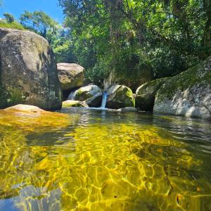 a body of water with rocks and a waterfall at Casa tia Rosa hospedagem familiar in Guapimirim