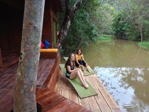 two women sitting on mats on a dock near a body of water at Harmony by the lake in Dambulla