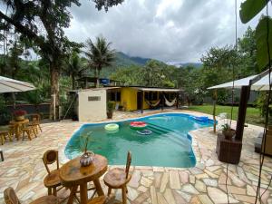 a pool with a table and chairs and a house at Chácara Paraíso Escondido in Angra dos Reis
