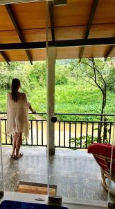 una donna in piedi su un balcone che guarda fuori da una finestra di Rainforest River Bay a Deniyaya